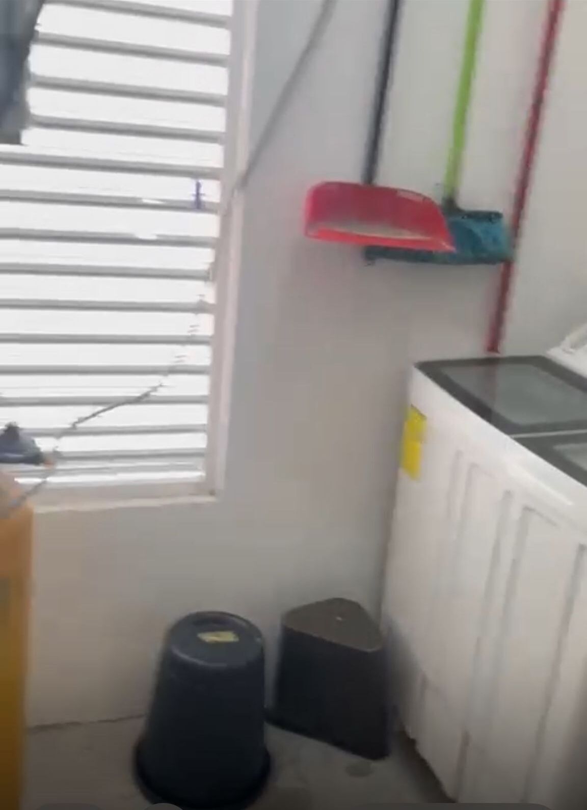 Een smalle gang met een raam aan de linkerkant, een radiator aan de rechterkant en een rode en blauwe plank erboven.