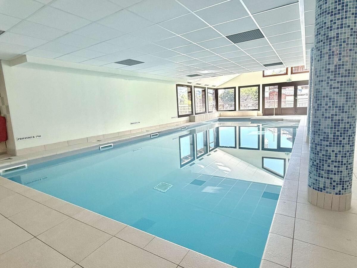 An indoor swimming pool with clear glass walls, tiled flooring, and a tiled column with a mosaic pattern.