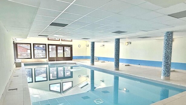 En indendørs swimmingpool med klart vand, fliserede vægge og et flisebelagt gulv.