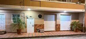 A two-story building with a white door, a window with metal bars, and two closed roller shutters. - Hostal la terraza sm (Santa Marta)