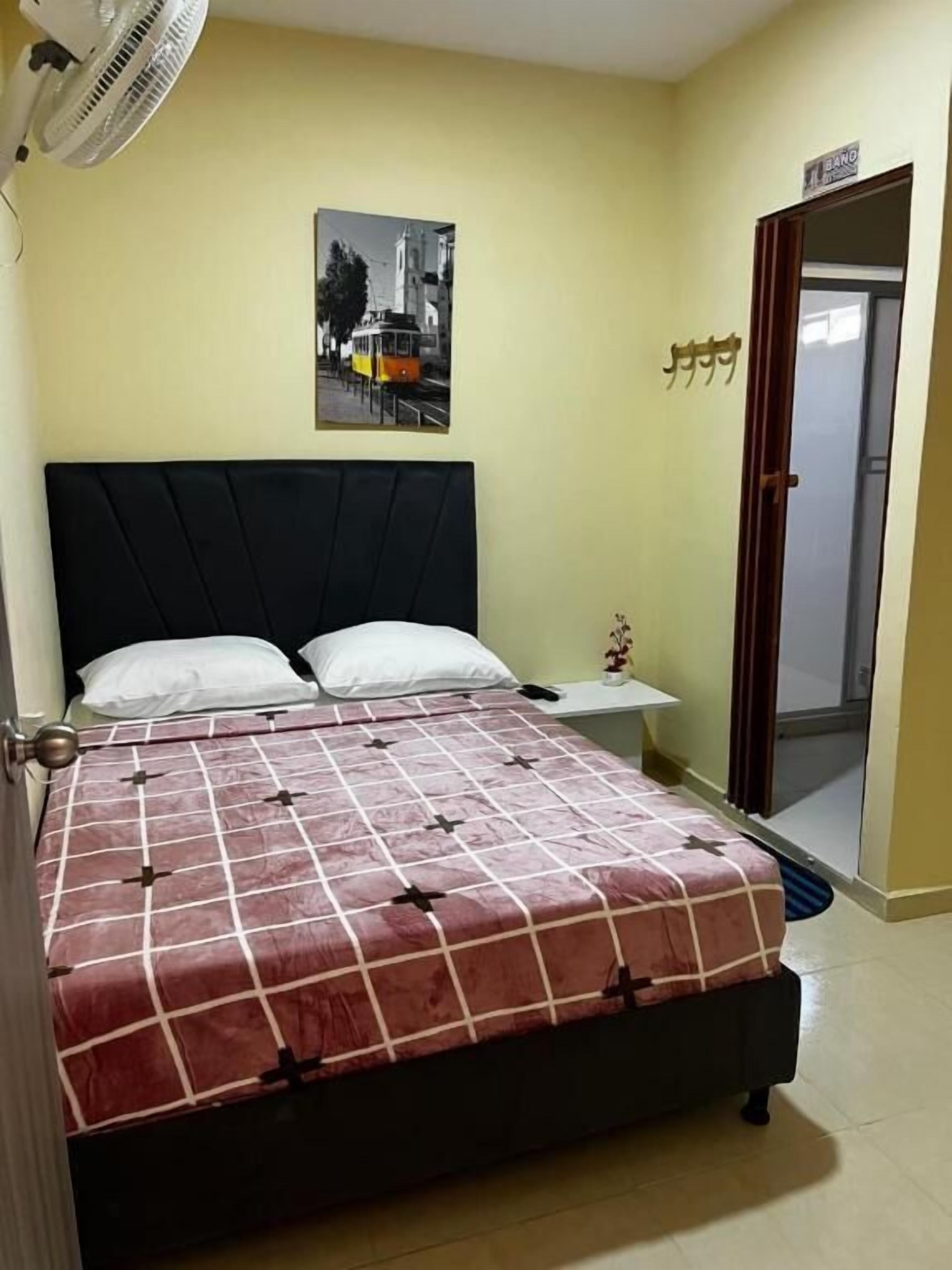 A bedroom with a bed, a nightstand, a wall-mounted fan, and a door with a sign.