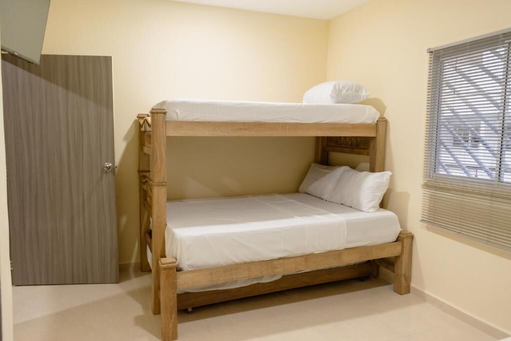 A bunk bed with white bedding in a room with beige walls and a window with blinds.