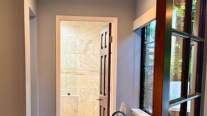 A hallway with a tiled floor, a door leading to a bathroom, and a window with a view of the outdoors.