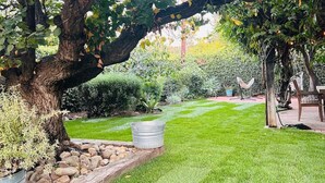 A well-maintained garden with a large tree, a grassy lawn, and a hammock.