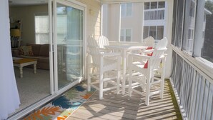 Une terrasse couverte avec une table et des chaises, une porte-fenêtre coulissante donnant sur le salon et une vue sur les maisons voisines.
