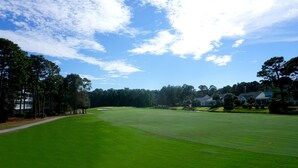 Un terrain de golf avec un ciel dégagé, des arbres et des maisons en arrière-plan.