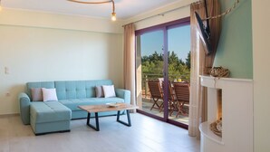 Ein Wohnzimmer mit einem hellblauen Sofa, einem Holztisch und einer Glastür, die auf eine Terrasse mit Holzmöbeln führt.
