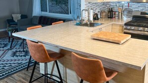 A modern kitchen with a central island, wooden cabinets, stainless steel appliances, and a dining area with two orange chairs. - Garden of the Gods Retreat - Upper Unit (Colorado Springs)