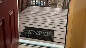 A wooden deck with a welcome mat, leading to a door with a view of a sunset over a mountainous landscape. - Garden of the Gods Retreat - Upper Unit (Colorado Springs)