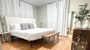 Ein modernes Schlafzimmer mit einem großen Bett, einer Holzbank, einem Nachttisch, einem Spiegel und einer Zimmerpflanze.