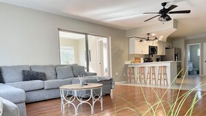 Ein modernes Wohnzimmer mit grauem Sofa, einem runden Couchtisch und einer Küchenzeile mit Bar und Hockern.