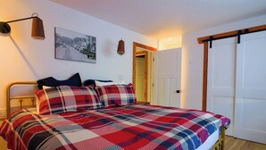Una cama con colcha de cuadros, una lámpara de pared y una puerta con marco de madera.