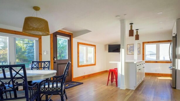 Una cocina con piso de madera, un comedor con una mesa redonda y sillas, y un refrigerador.