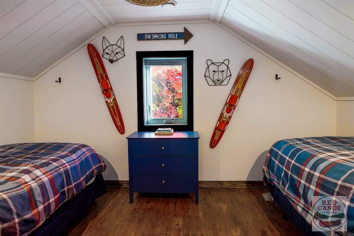 Een kamer met twee bedden, een kaptafel, een ingelijst foto en twee ski's aan de muur.