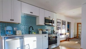 Una cocina moderna con armarios blancos, un protector contra salpicaduras azul, un microondas, un tostador y un horno.
