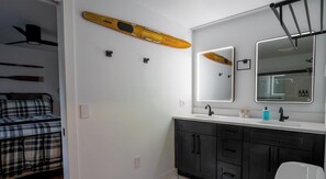 A modern bathroom with a large mirror, a wooden surfboard, and a ceiling fan.