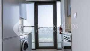 Eine moderne Küche mit eingebauter Waschmaschine, einem großen Fenster und einer Tür zum Balkon.