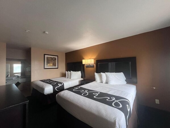 A hotel room with two beds, a desk, and a mirror.