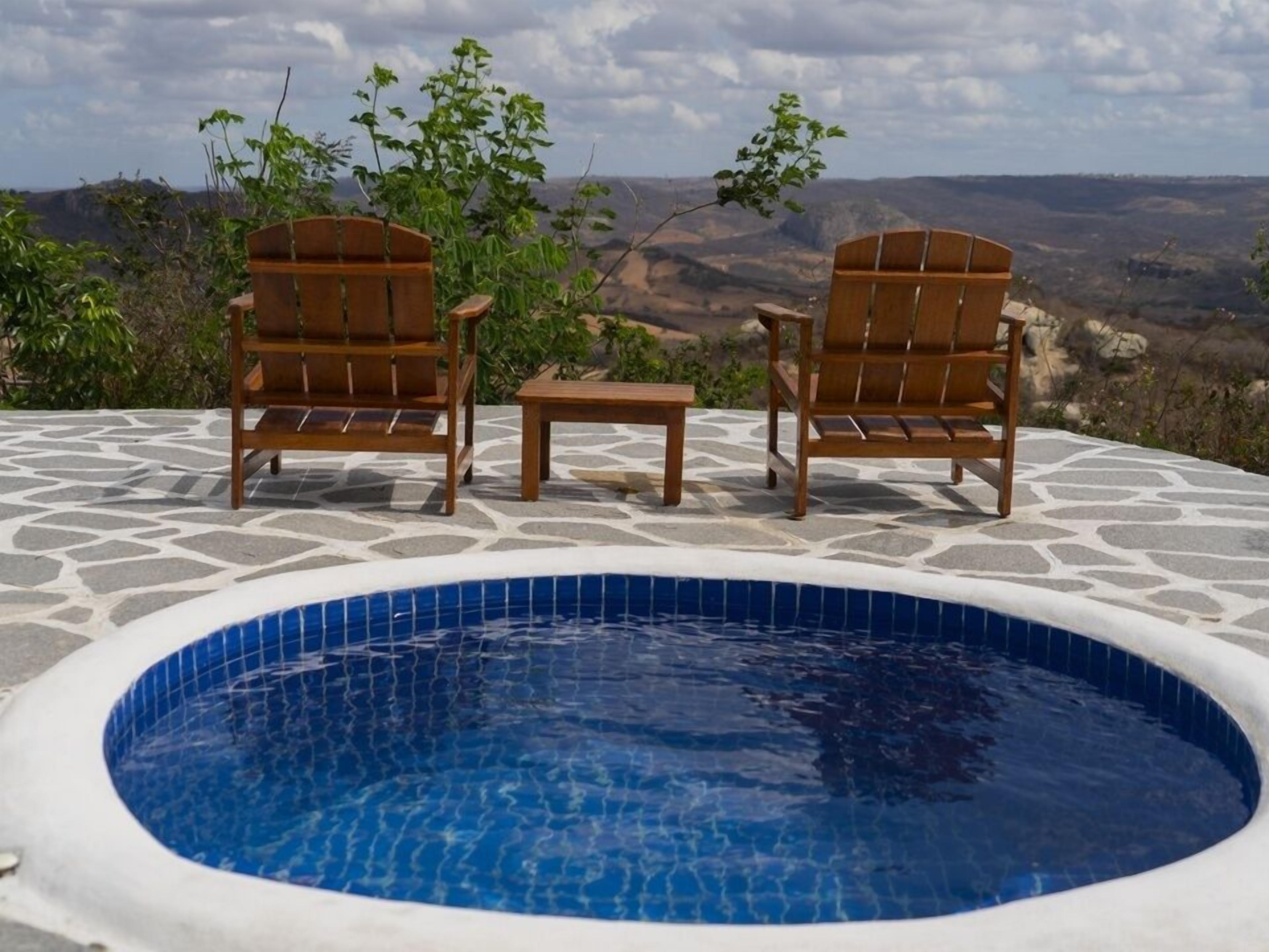 Piscina con dos sillas de madera y una pequeña mesa, rodeada de baldosas de piedra.
