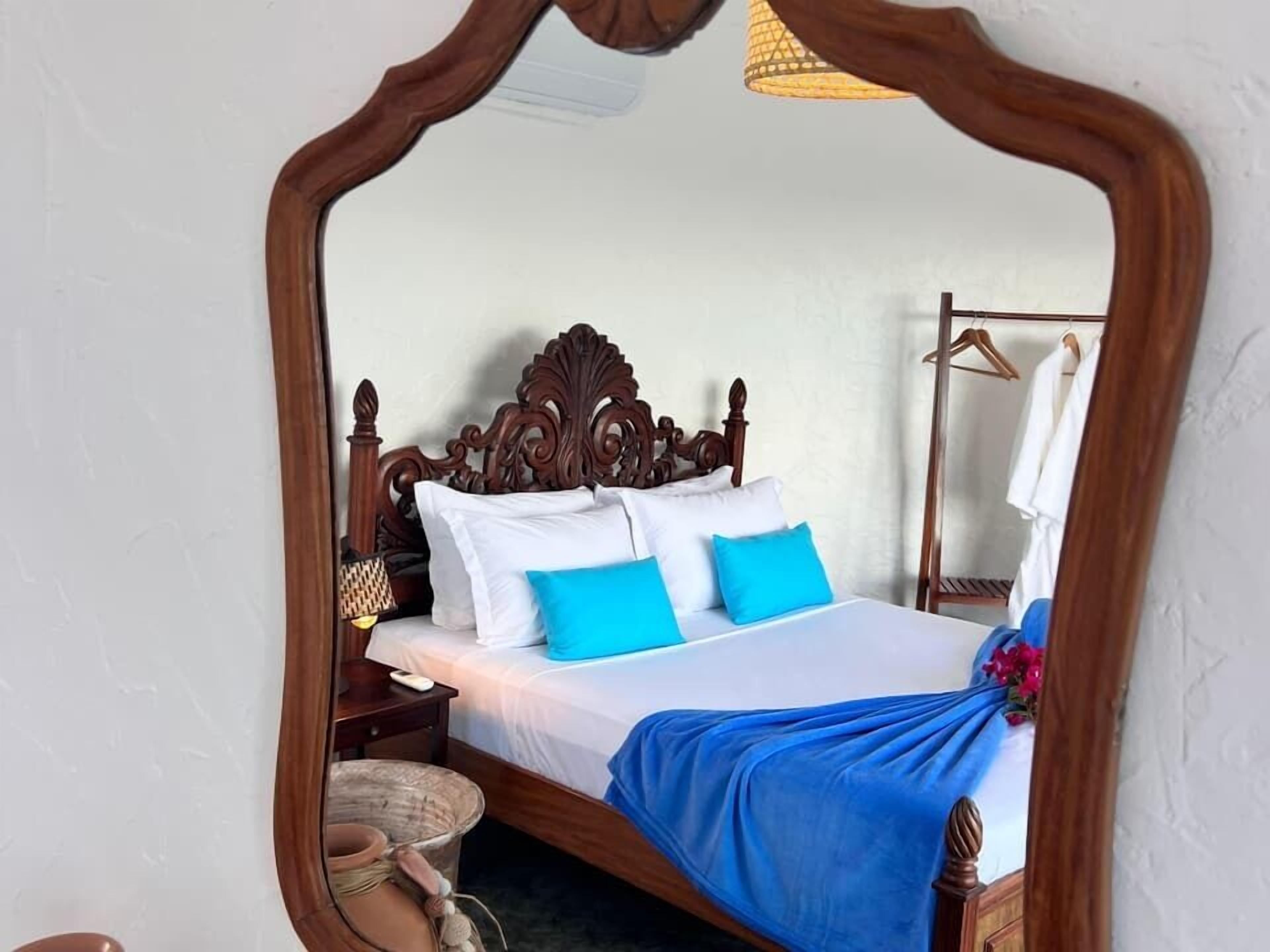 Un dormitorio con cama de madera, ropa de cama blanca y azul, una mesita de noche y una lámpara colgante.