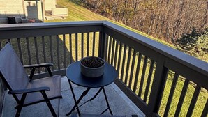 En balkon med to stole, et lille bord og en skål med fyrrenåle.