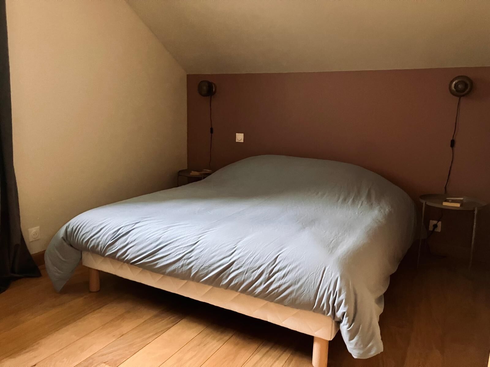 A single bed in a room with wooden flooring, a sloped ceiling, and two bedside lamps.