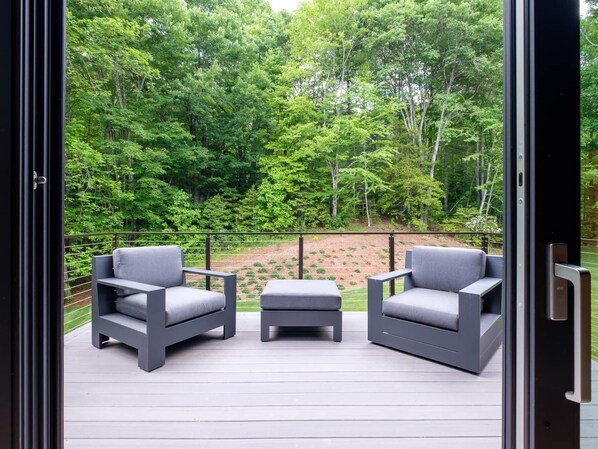 Un balcon avec deux chaises grises et une petite table, donnant sur une forêt verdoyante et luxuriante.
