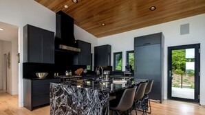 A modern kitchen with a marble island, black cabinetry, and a wooden ceiling. - Luxury Home - The Retreat House (Balsam Grove)