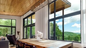 A modern dining area with a wooden table, purple upholstered chairs, and large windows offering a view of a forested landscape. - Luxury Home - The Retreat House (Balsam Grove)