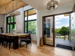 Ein moderner Essbereich mit Holztisch, Stühlen und einer Deckenleuchte. Große Fenster bieten Blick auf Grünflächen und einen Balkon.