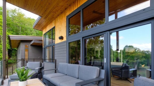 A modern outdoor living area with a gray sofa, a wooden table, and a potted plant. - Luxury Home - The Retreat House (Balsam Grove)