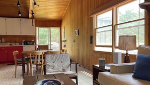 A cozy cabin interior with a dining area, a sofa, and a kitchen. - Island Retreat in Lonelyville (Bay Shore)