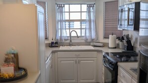Une cuisine de taille réduite avec des meubles blancs, un évier, une cuisinière et un four à micro-ondes.