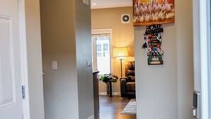 Un couloir avec un plancher en bois, un paillasson noir, une œuvre d’art accrochée au mur et une porte sur la gauche.