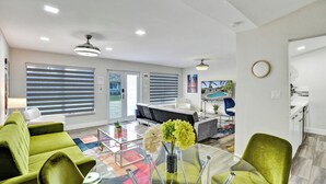 Una sala moderna con un sofá verde, una mesa de centro de vidrio y un comedor con un tapete colorido.