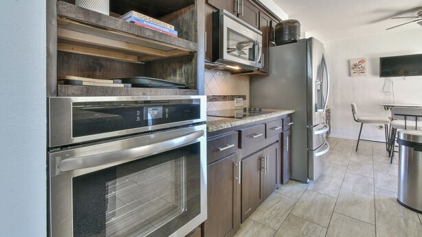Una cocina moderna con electrodomésticos de acero inoxidable, estantes de madera y un rebozado de azulejos.