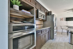 A modern kitchen with stainless steel appliances, wooden shelves, and a tiled backsplash. - Spacious Resort-Style Escape in Oklahoma City (Oklahoma City)