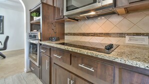 Una cocina con armarios de madera oscura, encimera de granito, microondas integrado y salpicadero con un diseño geométrico de azulejos.