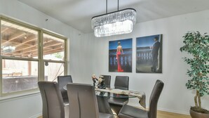 Un comedor con una mesa de vidrio, sillas de cuero, un candelabro y obras de arte en las paredes.