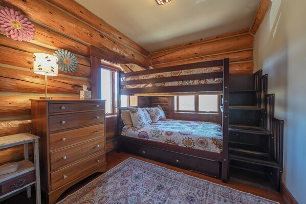 A wooden cabin bedroom with a bunk bed, a dresser, a lamp, and a patterned rug. - NEW! Private Mountain Cabin on 35 Acres - Endless Views (Crested Butte)