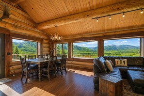 A log cabin interior with a dining area, leather sofa, and large windows offering a mountain view. - NEW! Private Mountain Cabin on 35 Acres - Endless Views (Crested Butte)