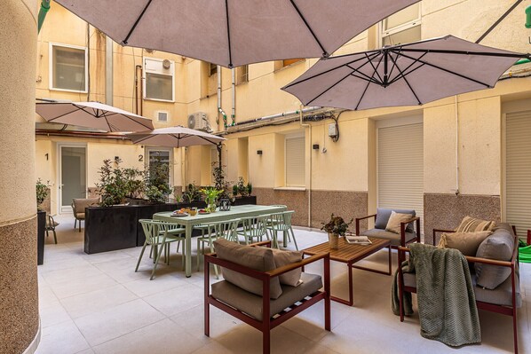 Ampio patio esterno con tavoli e sedie, ombreggiato da grandi ombrelloni e circondato da piante in vaso.