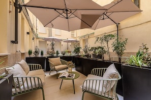 A cozy outdoor seating area with cushioned chairs and tables, surrounded by potted plants and umbrellas providing shade. - Waou Urban Home Chamberi VIII (Madrid)