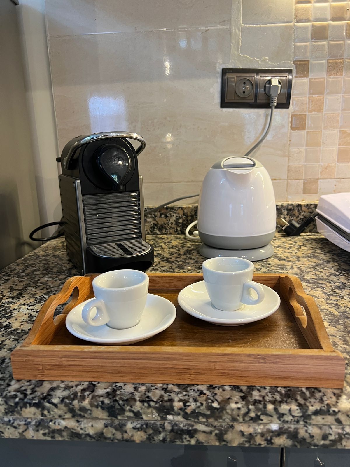 Eine Küchenarbeitsplatte mit einer Kaffeemaschine, einem Wasserkocher und zwei Tassen auf einem Tablett.