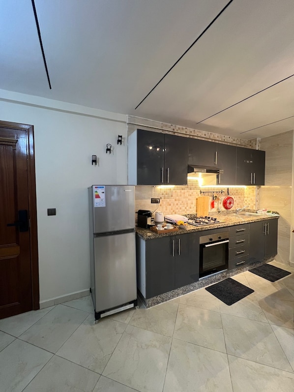 A modern kitchen with dark cabinets, a stainless steel refrigerator, and a tiled backsplash.