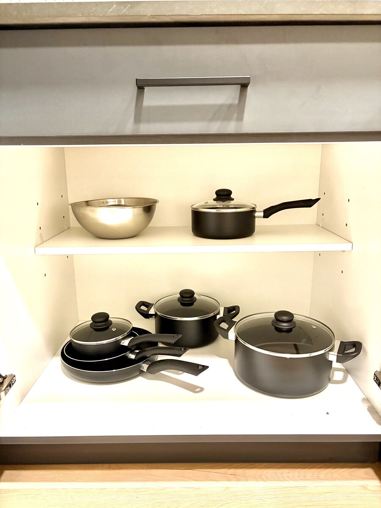 A kitchen with a white countertop, a stainless steel bowl, and several black pots and pans.