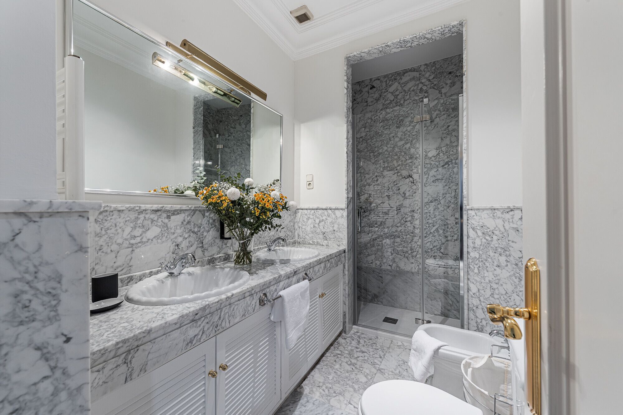 Une salle de bain moderne avec des comptoirs en marbre, un grand miroir, une douche avec une porte en verre et des toilettes.