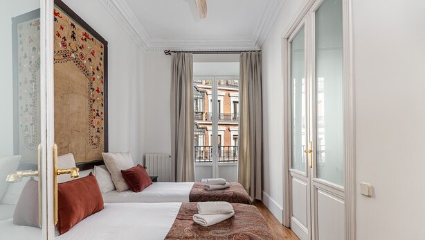 A hotel room with two beds, a large window with a view of buildings, and a patterned tapestry on the wall. - Waou Sol VII - Short Term Rental (Madrid)