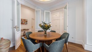A dining area with a round wooden table, six upholstered chairs, and a vase with flowers. - Waou Sol VII - Short Term Rental (Madrid)