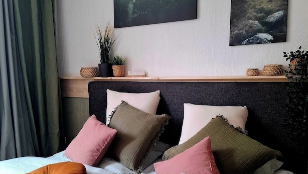A neatly arranged bedroom with a bed, pillows, a bedside table, and two wall-mounted paintings.